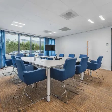Vergaderruimte met grote tafel en blauwe stoelen, perfect voor kantoorruimte huren op Hurksestraat 60 in Eindhoven De Hurk. Ruime kantoorpandomgeving met moderne faciliteiten voor zakelijke bijeenkomsten.