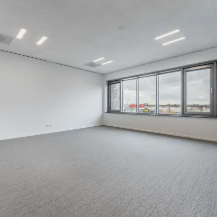 Ruime, heldere kantoorruimte te huur in Eindhoven De Hurk met groot raam en grijze vloerbedekking, ideaal voor het inrichten van moderne kantoren.