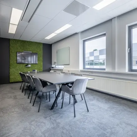 Vergaderruimte met lange tafel, omringd door stoelen, een scherm aan de muur en ramen die het kantoorpand lichte uitstraling geven aan Meerenakkerplein 1-10 in Eindhoven De Hurk.