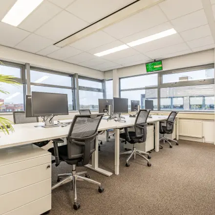 Kantoorruimte huren in Eindhoven De Hurk: moderne werkplek met bureaus, stoelen en computers, geschikt voor productief werken. Grote ramen bieden veel natuurlijk licht.