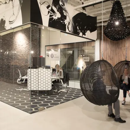 Moderne kantoorruimte huren in Eindhoven Strijp-S op Frederiklaan 10E met glazen wanden, stijlvolle meubels en decoratieve elementen. Personen voeren zakelijke activiteiten uit, zittend in designstoelen.