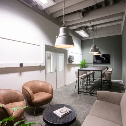 Moderne kantoorruimte huren in Eindhoven Strijp-S met stijlvolle zitplaatsen, hoge tafels en decoratieve planten voor een fris en uitnodigend interieur.