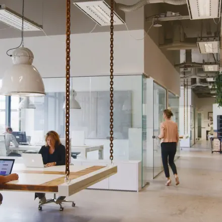 Moderne kantoorruimte in Eindhoven Strijp-S, met gemotiveerde professionals die bezig zijn met werk aan laptops. De inrichting is industrieel met grote ramen en hangende verlichting.