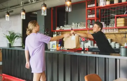 In een moderne kantooruimte op Torenallee 20, Eindhoven, overhandigt een medewerker een papieren zak aan een klant bij de balie, omringd door industriële elementen.