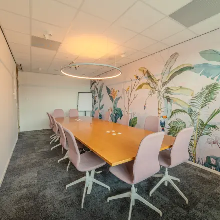 Vergaderruimte met grote houten tafel en zachte stoelen op Torenallee 20, Eindhoven Strijp-S, ideaal voor kantoorruimte huren. Tropische accentmuur biedt een creatieve touch.