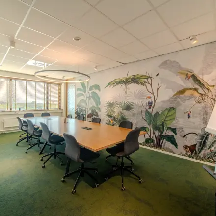 Vergaderruimte met grote houten tafel en acht stoelen op Torenallee 20 in Eindhoven Strijp-S. De muren zijn versierd met een plantenmotief, ideaal voor wie een kantoorpand wil huren.
