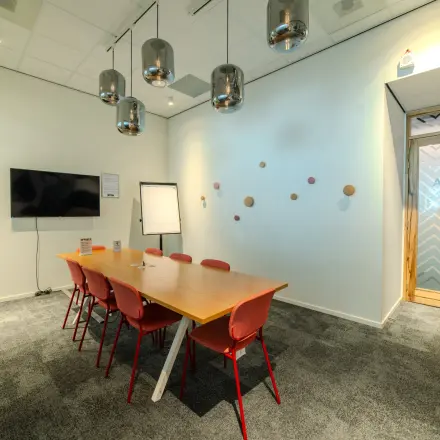 Vergaderruimte met een houten tafel en zes rode stoelen, TV aan de wand en speelse decoratie in een kantoorpand aan Torenallee 20, Eindhoven Strijp-S.