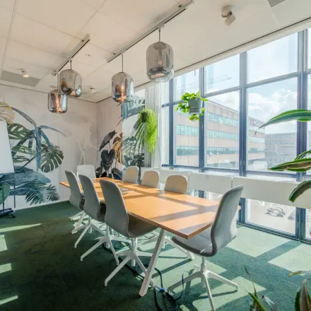 Heldere vergaderruimte op Torenallee 20, Eindhoven Strijp-S, met grote ramen, groene accenten en een lange houten tafel om te huren als kantoorruimte.