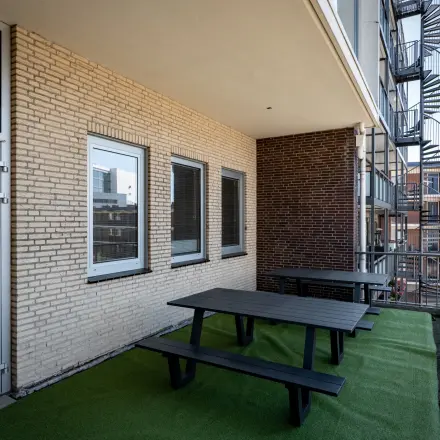 Balkon van een kantoorpand op Kuipersdijk 2-4 in Enschede met groene vloerbedekking en zwarte picknicktafels. Aan de buitenkant zijn bakstenen muren zichtbaar en een wenteltrap naar boven.