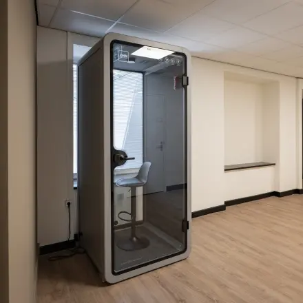 Kantoorruimte op Kuipersdijk 2-4 in Enschede met een moderne werkplekvoorziening en houten vloer. Het interieur is vrij minimalistisch met een stijlvolle telefoniecabine voor privégesprekken.