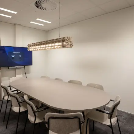 Moderne vergaderruimte in het kantoorpand op Kuipersdijk 2-4, Enschede, met een lange tafel omringd door stoelen en een digitale presentatiescherm. Ideaal voor bedrijven die kantoorruimte willen huren.