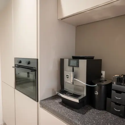Moderne kitchenette in een kantoorpand op Kuipersdijk 2-4, Enschede, voorzien van een hoogwaardige koffiemachine en opbergmogelijkheden.