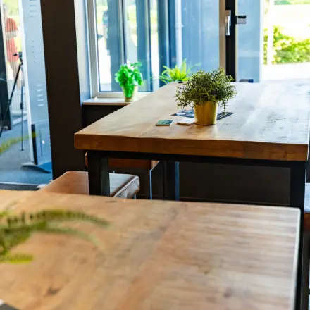 Moderne kantoorruimte in Enschede met houten tafels en hoge krukken bij grote ramen, voor een inspirerende werkplek in het kantoorpand op Marssteden 20. Ideaal voor kantoorruimte huren.