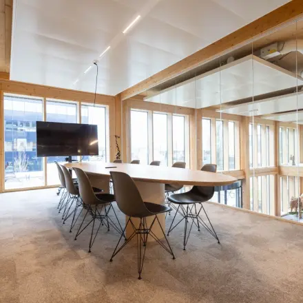 Moderne vergaderruimte in het kantoorpand op Moutlaan 1-23, Enschede, met grote ramen, houten afwerking en een grote tafel omgeven door stoelen. Perfect om een kantoorruimte te huren.