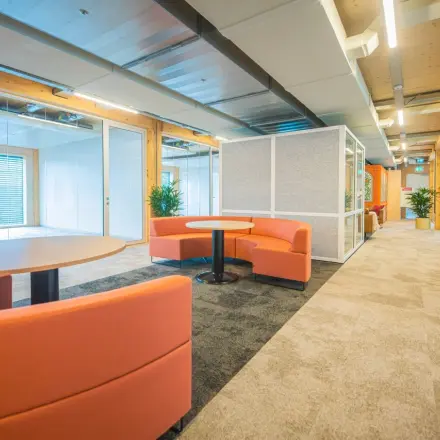 Moderne kantoorruimte in Enschede met kleurrijke zitbanken, tafels en veel lichtinval. Perfect voor ondernemers die een kantoorpand willen huren.