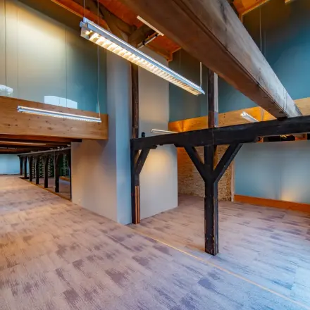 Kantoorruimte huren op Prins Hendrikkade 3, Franeker met een ruimtelijk interieur en houten balken. De ruimte oogt licht dankzij grote ramen en moderne verlichting, geschikt voor diverse kantooropstellingen.