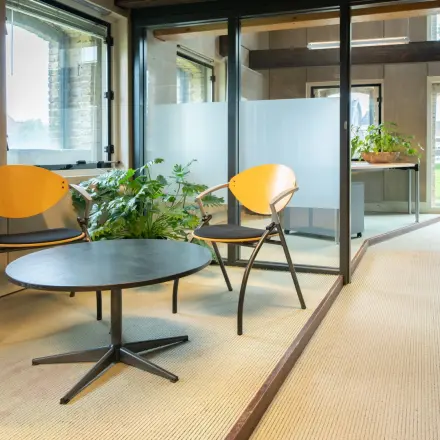Kantoorruimte huren op Prins Hendrikkade 3 in Franeker met moderne inrichting, inclusief glazen wanden, houten stoelen en groene planten, geschikt voor diverse werkdoeleinden.