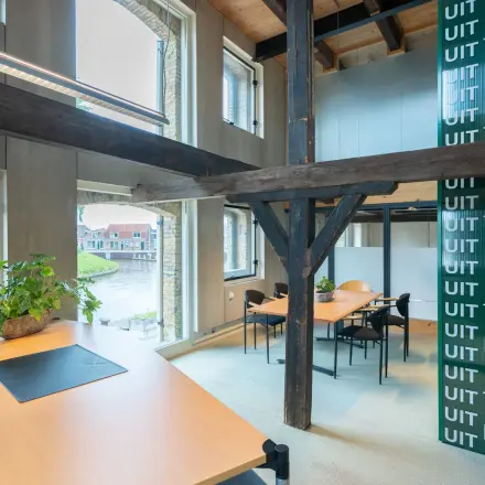 Kantoorruimte op de eerste verdieping van een kantoorpand aan Prins Hendrikkade 3 in Franeker, voorzien van houten balken, grote ramen, en diverse werkplekken met bureaus en stoelen.