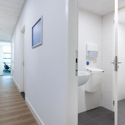Kantoorcorridor met houten vloer, witte muren en een toilet aan de rechterkant op Groningenweg 8 8, Gouda. Perfect om een kantoorruimte te huren.