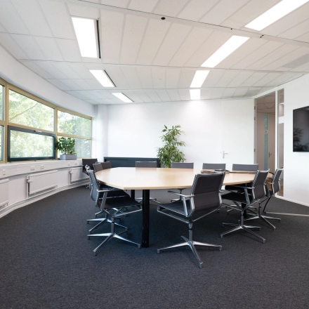 Vergaderruimte met grote tafel en stoelen, lichte omgeving met ramen en planten, ideaal voor kantoorruimte huren in kantoorpand op Groningenweg 8 8, Gouda.