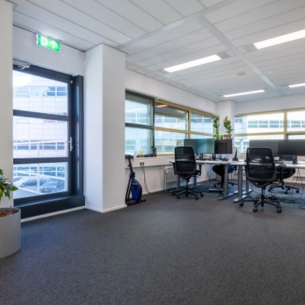 Heldere kantoorruimte met vier bureaus, stoelen en een plant in een kantoorpand op Groningenweg 8 8 in Gouda. Grote ramen zorgen voor veel licht. Ideaal voor wie kantoorruimte wil huren.