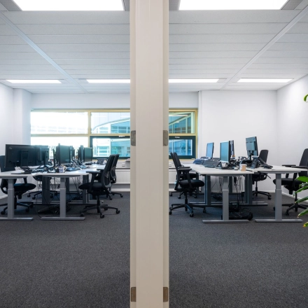 Moderne kantoorruimte in Gouda met meerdere bureaus en computers, geschikt voor zakelijke activiteiten. Grote ramen zorgen voor natuurlijk licht in het kantoorpand.