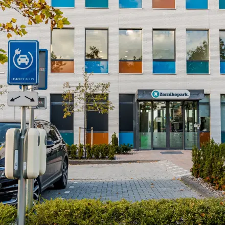 Vooraanzicht van het kantoorpand aan Zernikepark 12 in Groningen met kleurrijke raampartijen en laadpunt voor elektrische auto's.