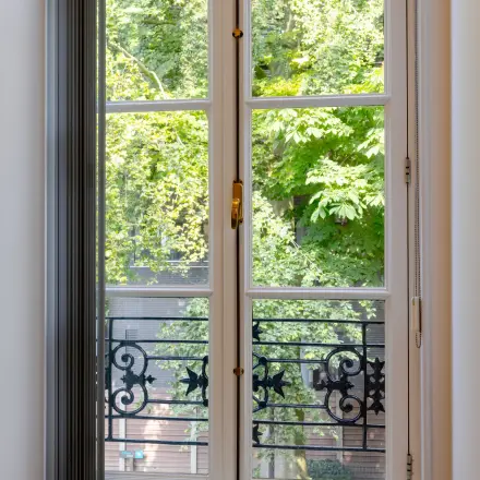 Uitzicht door een groot raam met smeedijzeren balkon, groene bomen buiten. Ideaal voor kantoorruimte huren in Haarlem Centraal Station, Kennemerplein 20.