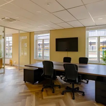 Moderne kantoorruimte te huur op Kennemerplein 20 in Haarlem Centraal Station met grote vergadertafel, stoelen en glazen wanden, ideaal voor zakelijke bijeenkomsten.