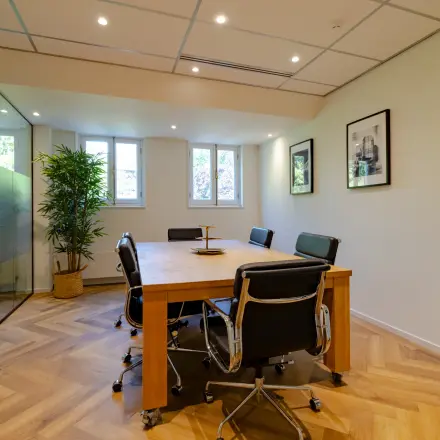 Stijlvol kantoorpand op Kennemerplein 20 in Haarlem Centraal Station, met vergadertafel en zwarte stoelen voor kantoorruimte huren. Houten vloer en kunst aan de muur creëren een warme sfeer.