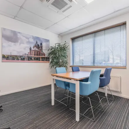 Stijlvolle vergaderruimte in kantoorpand Steenovenweg 5, Helmond. De ruimte is voorzien van moderne stoelen rondom een houten tafel, met uitzicht door een groot raam.