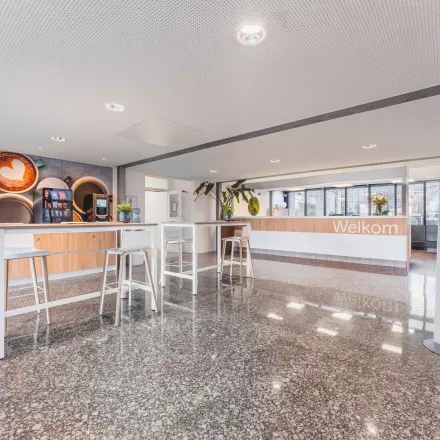 Lichte en ruime receptie met moderne houten balie en hoge tafels, geschikt voor informele ontmoetingen. Perfecte locatie voor kantoorruimte huren aan Steenovenweg 5 in Helmond.