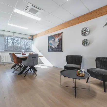 Kantoorruimte te huur aan Steenovenweg 5 in Helmond met een stijlvolle inrichting, waaronder een vergadertafel, stoelen en decoratieve elementen. Grote ramen bieden natuurlijk licht.