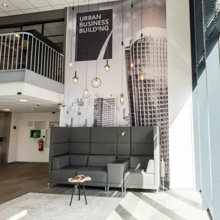 In het kantoorpand op Demmersweg 3, Hengelo, een moderne loungehoek met hoge grijze bank en industriële verlichting. Zoek je kantoorruimte te huur? Hier vind je inspiratie en comfort.