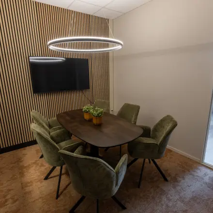 Moderne vergaderruimte met zes groene stoelen rondom een houten tafel, LED-verlichting en een flatscreen aan de wand. Ideale kantoorruimte huren op Lansinkesweg 4, Hengelo.