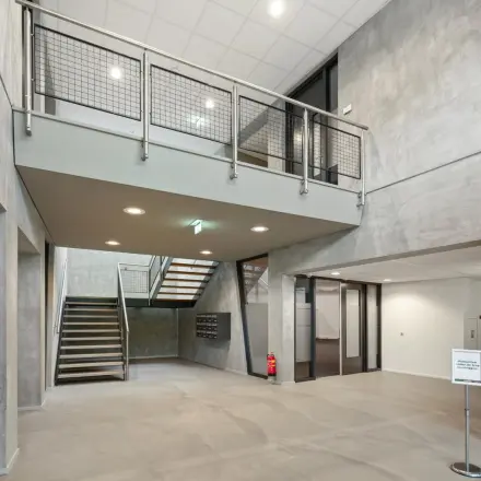 Entree van modern kantoorpand op Lintelerweg 40, Hengelo. Ruime hal met industriële uitstraling en zicht op de trap. Ideaal voor bedrijven die kantoorruimte willen huren.