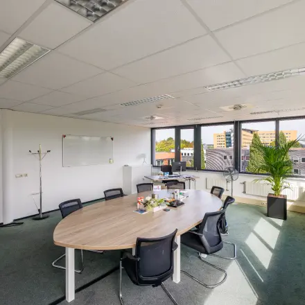 Lichte kantoorruimte op Welbergweg 60, Hengelo met grote ramen, een ovale tafel, stoelen en een whiteboard. Ideaal voor kantoorruimte huren in een kantoorpand. Ruimte is gemeubileerd en klaar voor gebruik.