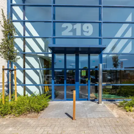 Ingang van een modern kantoorpand op Franciscusweg 219 in Hilversum, met grote glazen gevel en entree.