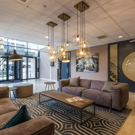 Stijlvolle ontvangstruimte binnen kantoorpand Marathon 2 in Hilversum, met comfortabele banken, moderne verlichting en decoratieve elementen. Perfect voor wie een kantoorruimte wil huren.