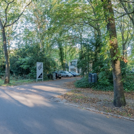 Buitenzicht op het kantoorpand gelegen aan de groene Mozartlaan 25 in Hilversum, omgeven door bomen en met een parkeerplaats vooraan.