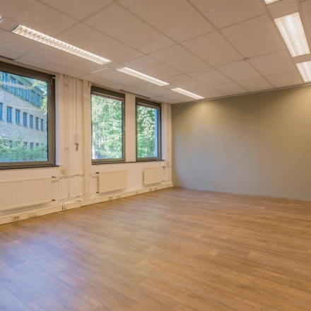 Lichte en ruime kantoorruimte te huur op Mozartlaan 25, Hilversum, met grote ramen en houten vloer, ideaal voor een open werkruimte.