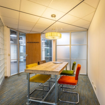 Vergaderruimte in kantoorpand op Mozartlaan 25 in Hilversum met houten tafel en kleurrijke stoelen, ideaal voor wie kantoorruimte wil huren.