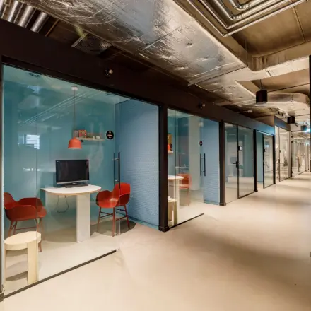 Moderne kantoorruimte op Siriusdreef 16 in Hoofddorp met glazen werkplekken, ideaal om kantoren te huren. Het interieur heeft glazen wanden en rode stoelen, wat een professionele uitstraling geeft.