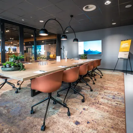 Moderne vergaderruimte in een kantoorpand op Bargelaan 200 in Leiden met houten tafel, oranje stoelen en sfeervolle verlichting.