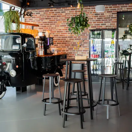 Unieke kantoorruimte te huur in Leiden, Bargelaan 200, met een stijlvolle bar en vintage koffieauto, omringd door hoge krukken en hangende planten.