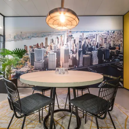 Kantoorruimte huren aan de Bargelaan 200 in Leiden met sfeervolle vergaderruimte, voorzien van ronde tafel, stoelen en stedelijke muurschildering voor een inspirerende werkomgeving in een modern kantoorpand.