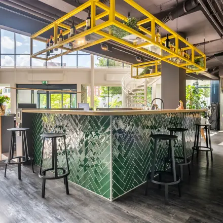 Moderne kantoorruimte op Kanaalpark 140 in Leiden met een stijlvolle bar, groene tegels en gele accenten. Ruim, met veel natuurlijk licht en zitmogelijkheden.