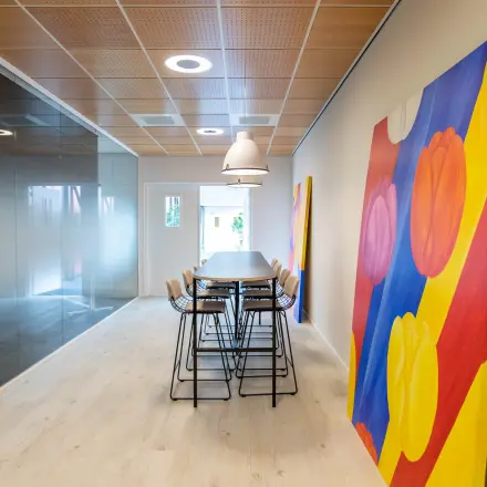 Modern kantoorpand op Pompoenweg 3 - 15 in Leiden met kleurrijke kunst, hoge stoelen en glazen wanden.
