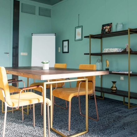 Stijlvolle kantoorruimte met groene muren, een vergadertafel en vijf gele stoelen bij Blankenstein 400 in Meppel, ideaal om te huren.