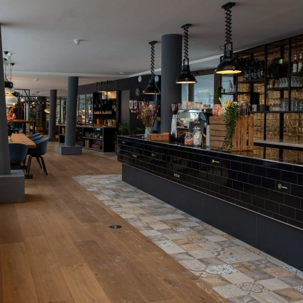 Moderne kantoorruimte in Meppel met lange tafels, sfeervolle verlichting en een stijlvolle zwarte balie, ideaal voor huur.